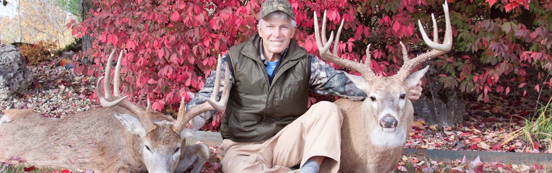 Deer Hunter Kneeling with Two Bucks